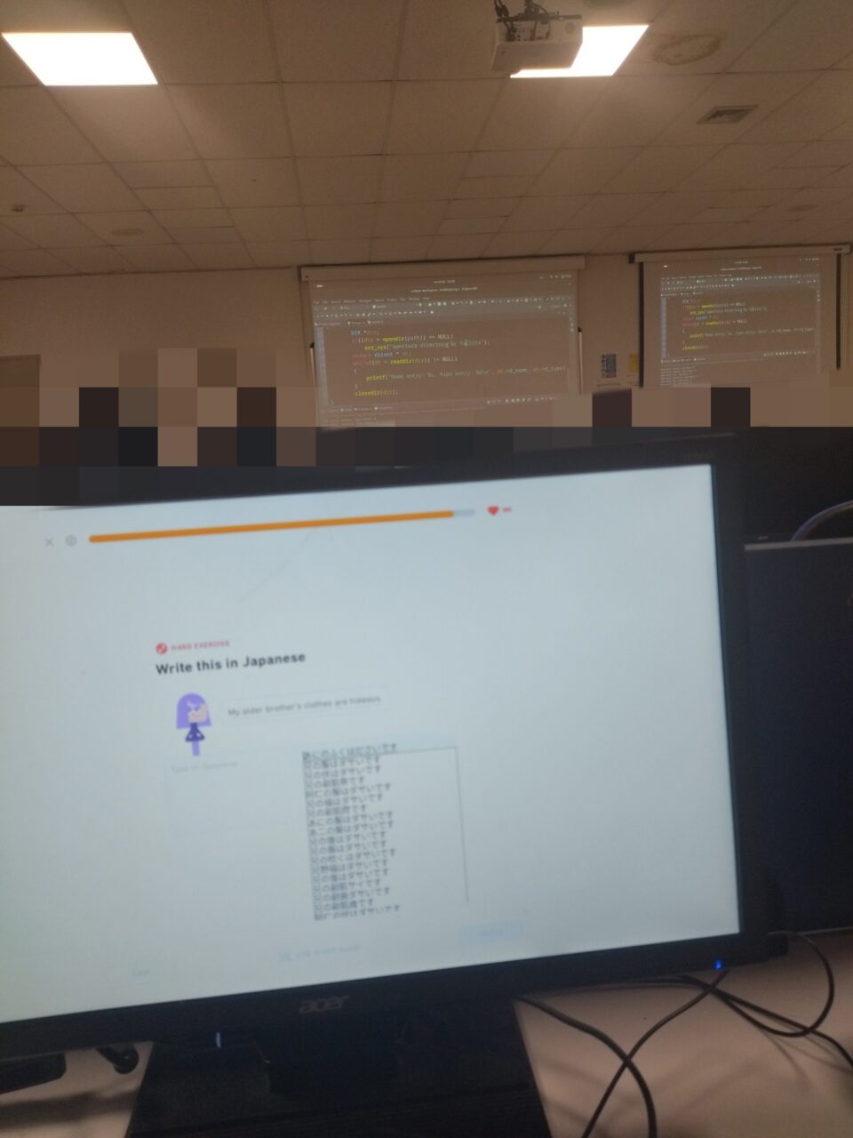 In laboratorio, il proiettore in fondo mostra il codice C, il mio monitor un esercizio di Duolingo